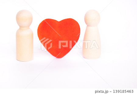 Two wooden figurines positioned on either side of a red heart shape, set against a clean white background, symbolizing connection and relationships Two wooden figurines positioned on either side of a red heart shape, set against a clean white background, symbolizing connection and relationships 139185463