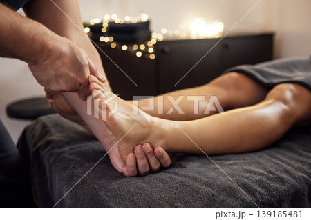 Male therapist providing a foot massage to a relaxed client on a massage table, surrounded by soft lighting and a calming atmosphere, promoting relaxation and wellness 139185481