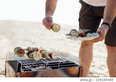 A young man in a summer casual outfit is having a barbecue on beach. A young man in a summer casual outfit is having a barbecue on beach. 139185489
