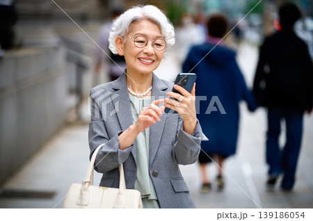 街中でスマートフォンを操作し笑顔を見せるシニア女性 街中でスマートフォンを操作し笑顔を見せるシニア女性 139186054