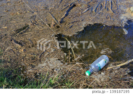 Plastic bottle discarded in shallow river water near the grassy bank. Environmental pollution and water contamination concept. 139187195