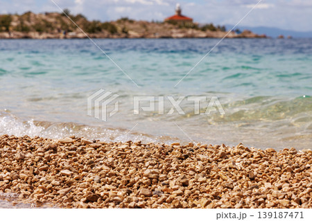 Pebble beach with clear turquoise sea and distant rocky shore in blurred background. Adriatic sea coast in Makarska, Croatia with copy space. Selective focus Pebble beach with clear turquoise sea and distant rocky shore in blurred background. Adriatic sea coast in Makarska, Croatia with copy space. Selective focus 139187471