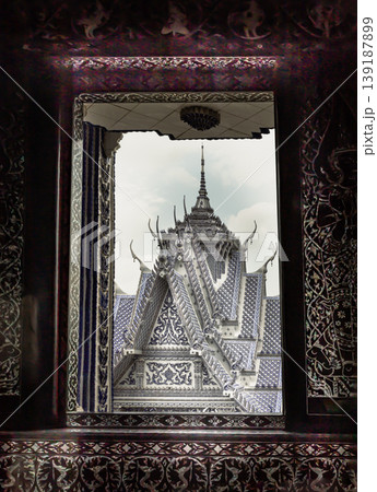 Looking through a dark, intricately patterned portal, the eye is drawn to the luminous peaks of the sanctuary, which rise like a ceramic mirage against the pale sky of Wat Paknam Kham Nu "Blue 139187899