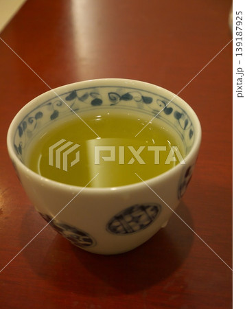 木目調のテーブルに置かれた、唐草模様の湯呑みに入った緑茶 木目調のテーブルに置かれた、唐草模様の湯呑みに入った緑茶 139187925