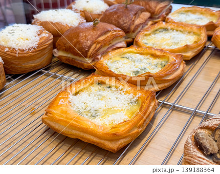 Savory pastry squares with cheese filling and grated topping placed on metal rack in bakery. Snack preparation, food service, baked goods assortment and culinary display concept. Savory pastry squares with cheese filling and grated topping placed on metal rack in bakery. Snack preparation, food service, baked goods assortment and culinary display concept. 139188364