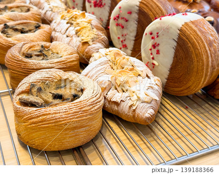 Croissants and laminated pastries with chocolate filling, almond flakes and white chocolate coating displayed on rack. Bakery assortment, artisan baking, dessert variety and confectionery presentation Croissants and laminated pastries with chocolate filling, almond flakes and white chocolate coating displayed on rack. Bakery assortment, artisan baking, dessert variety and confectionery presentation 139188366