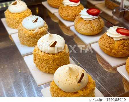 Assorted cream filled pastries with strawberry topping arranged on display trays. Bakery assortment, dessert variety, pastry craftsmanship, and retail food presentation. Assorted cream filled pastries with strawberry topping arranged on display trays. Bakery assortment, dessert variety, pastry craftsmanship, and retail food presentation. 139188440