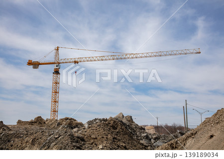 Tower crane at construction site with dirt mounds and cloudy blue sky Tower crane at construction site with dirt mounds and cloudy blue sky 139189034