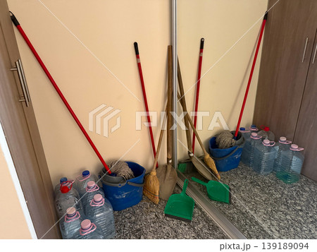 Cleaning tools and water containers stored in a small interior space. Household maintenance, sanitation routine, storage organization, and domestic utility area. Cleaning tools and water containers stored in a small interior space. Household maintenance, sanitation routine, storage organization, and domestic utility area. 139189094