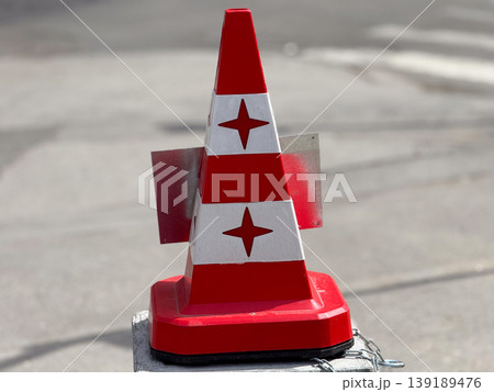 Red and white traffic cone with reflective panels on street surface. Road safety, construction warning, urban infrastructure, and hazard signaling in city environment. Red and white traffic cone with reflective panels on street surface. Road safety, construction warning, urban infrastructure, and hazard signaling in city environment. 139189476