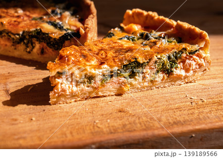 Close-up of a slice of French quiche on a wooden board, delicious traditional pastries in bright sunlight from a window, delicious homemade pastries Close-up of a slice of French quiche on a wooden board, delicious traditional pastries in bright sunlight from a window, delicious homemade pastries 139189566