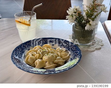 Plate of dumplings with drink and flower vase on marble table in cafe interior setting. Dining experience, food styling, hospitality service, casual meal and aesthetic composition. Plate of dumplings with drink and flower vase on marble table in cafe interior setting. Dining experience, food styling, hospitality service, casual meal and aesthetic composition. 139190199