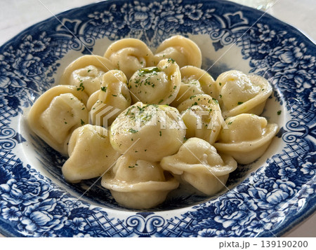 Plate of dumplings with butter and herbs served on blue patterned dish in restaurant setting. Russian cuisine, food presentation, lunch meal, comfort eating and gastronomy culture. Plate of dumplings with butter and herbs served on blue patterned dish in restaurant setting. Russian cuisine, food presentation, lunch meal, comfort eating and gastronomy culture. 139190200