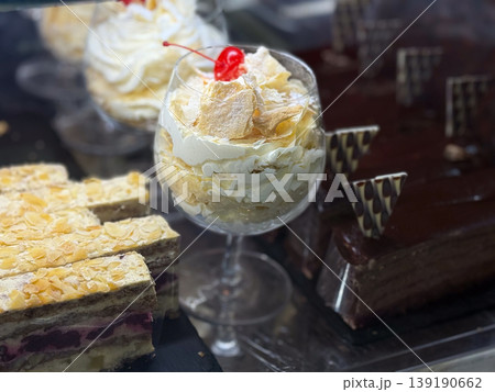 Cream dessert served in glass with cherry topping in bakery display. Sweet presentation, layered texture, confectionery detail, indulgent treat, and cafe dessert offering. Cream dessert served in glass with cherry topping in bakery display. Sweet presentation, layered texture, confectionery detail, indulgent treat, and cafe dessert offering. 139190662