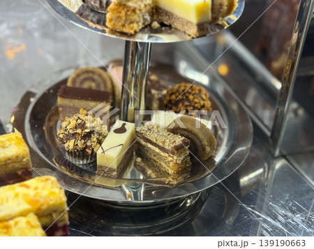 Tiered metal stand with assorted pastries and cakes in bakery setting. Dessert presentation, confectionery assortment, layered serving, sweet selection, and catering display concept. 139190663
