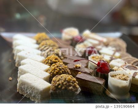 Assorted small pastries and sweets arranged on tray in bakery showcase. Dessert variety, confectionery selection, texture diversity, sweet assortment, and retail food display concept. 139190664