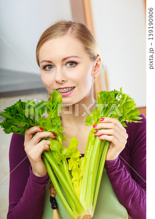 Woman in kitchen holds green celery Woman in kitchen holds green celery 139190906