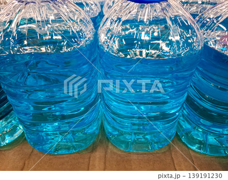 Several large plastic bottles filled with bright blue liquid are arranged in a row. The setting shows a clear surface under good lighting. The bottles are neatly organized. 139191230