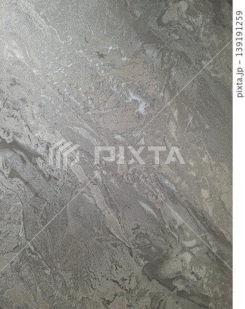 A brushed silver metallic surface displays a wavy texture with reflections. Light hits the surface, creating shiny patterns and variations in depth and tone. A brushed silver metallic surface displays a wavy texture with reflections. Light hits the surface, creating shiny patterns and variations in depth and tone. 139191259