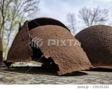 Close up view of old military helmets with rust and signs of wear. These helmets lie on a rough surface, highlighting their history and showing the effects of time and weather. 139191262