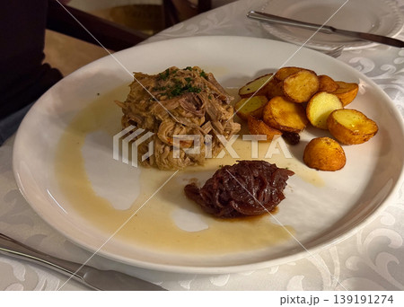 Braised shredded meat served with roasted potatoes and caramelized onion on a white restaurant plate. Comfort food, rustic cuisine, dinner portion, savory flavor, and traditional meal service. 139191274