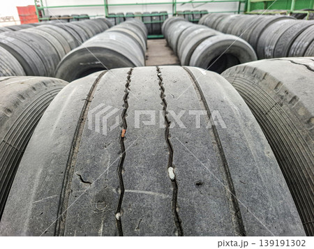 Wheels are stacked in rows inside a warehouse. The tires show signs of wear and are waiting to be removed. This area is used for storage and management of old tires. 139191302