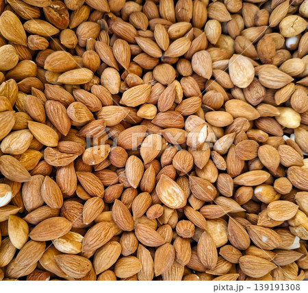 A collection of apricot kernels is displayed on a flat surface. The small seeds show different shapes and colors under natural light. Each kernel has its own unique texture and appearance. 139191308