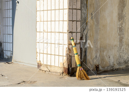 traditional sorghum broom leans against the corner of a building with white tiles and a shabby wall 139191525