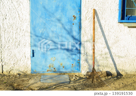 fan rake stands against a white wall of a house next to a blue metal door in the garden 139191530