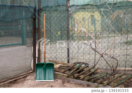 green plastic snow shovel leaning against a wire mesh fence in the garden area during spring 139191533