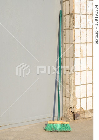 long brush with green bristles stands in the corner by a gray door and tiled wall outside 139191534