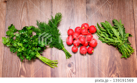 top view of laid out bunches of greens and a pile of radishes on a dark wooden surface 139191569