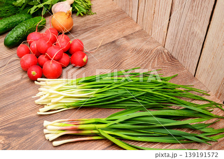bunches of green onions and garlic next to a pile of radishes on a brown wooden surface 139191572