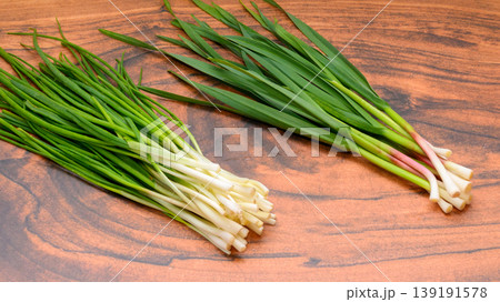two different types of green onions on a wooden table background two different types of green onions on a wooden table background 139191578