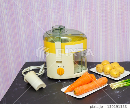 beige juicer on the table next to washed potatoes, carrots and green onions beige juicer on the table next to washed potatoes, carrots and green onions 139191588