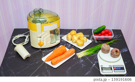 large set of vegetables including beets and cucumbers next to a juicer and scales on the table 139191606