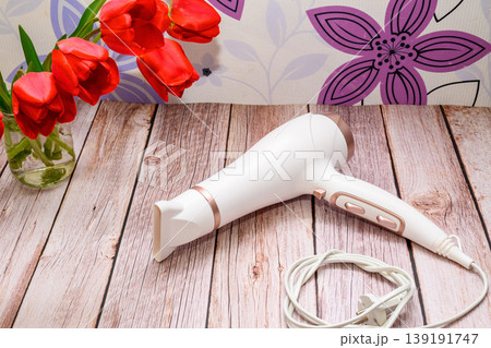 modern hair dryer on a wooden table with red tulips in the background modern hair dryer on a wooden table with red tulips in the background 139191747