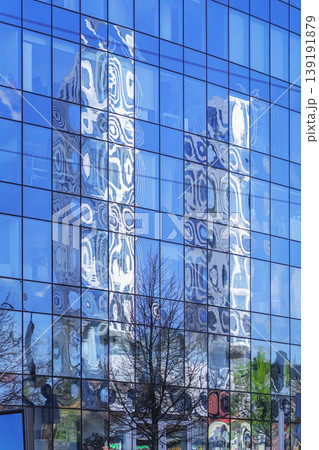 Glass facade with blue window grid with reflection of towers, tree silhouettes, urban architecture. Abstract blurred urban reflection, business, city design, corporate exterior, real estate background 139191879