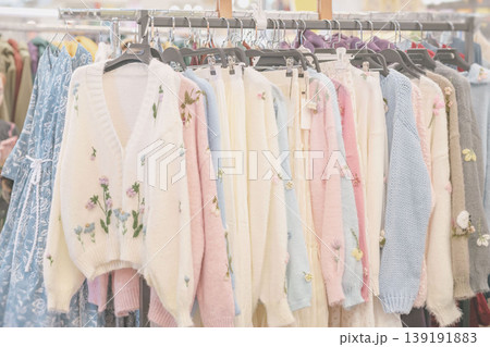 Clothing rack displays knit cardigans, sweaters, dresses, hangers, and floral embroidery in retail store. Concept of handmade clothing, boutique fashion, shopping, wardrobe, textile, apparel sales Clothing rack displays knit cardigans, sweaters, dresses, hangers, and floral embroidery in retail store. Concept of handmade clothing, boutique fashion, shopping, wardrobe, textile, apparel sales 139191883