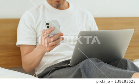 ベッドでパソコンとスマートフォンを使う男性の手元 ベッドでパソコンとスマートフォンを使う男性の手元 139193625