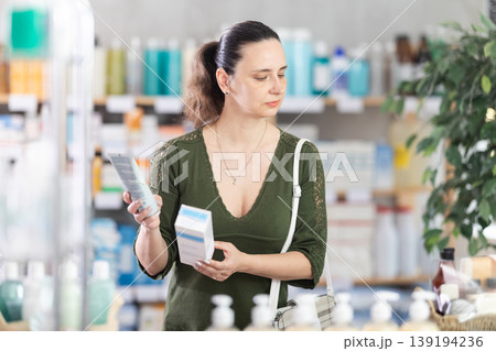 woman carefully chooses a cream at the pharmacy woman carefully chooses a cream at the pharmacy 139194236