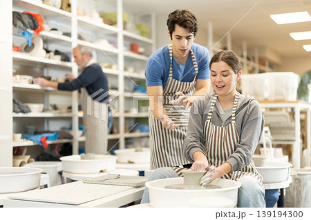 Young man helping young woman shape pottery on wheel Young man helping young woman shape pottery on wheel 139194300