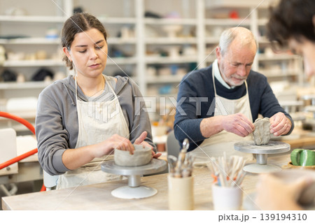 During working day, three pottery workshop workers sculpt from clay, form final product 139194310