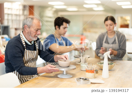 Eldery man sculpts ceramic piece in workshop 139194317