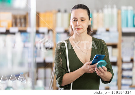 Middle-aged woman customer scanning QR-code on cosmetics Middle-aged woman customer scanning QR-code on cosmetics 139194334