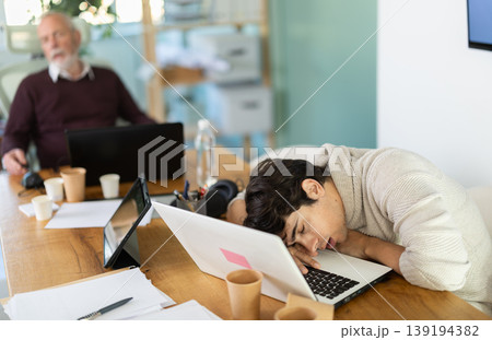 Tired male office workers having nap while sitting in workplace Tired male office workers having nap while sitting in workplace 139194382