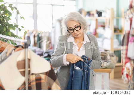 Mature woman standing in store and choosing jeans Mature woman standing in store and choosing jeans 139194383