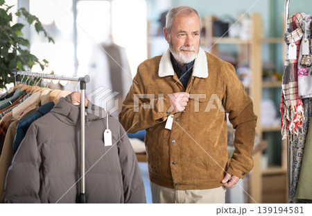 Elderly man trying on brown jacket in store Elderly man trying on brown jacket in store 139194581
