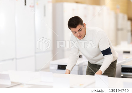 Guy choose modern washing machine or dishwasher at supermarket Guy choose modern washing machine or dishwasher at supermarket 139194740