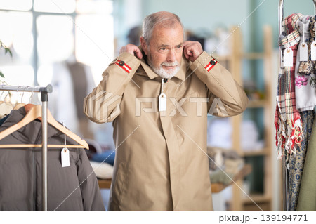 Mature male customer is trying on raincoat during shopping in store Mature male customer is trying on raincoat during shopping in store 139194771